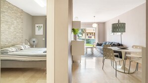 Ein modernes Wohnzimmer mit einem Bett, einem Esstisch und Stühlen. Auf dem Tisch befinden sich eine Pflanze und eine Lampe.