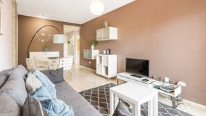 Ein modernes Wohnzimmer mit einer Couch, einem Fernseher und einem Essbereich mit Stühlen und einem Tisch.