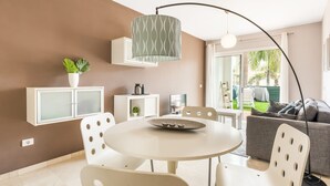 Ein modernes Wohnzimmer mit einem runden Esstisch, weißen Stühlen, einem grauen Sofa und einer Deckenleuchte.