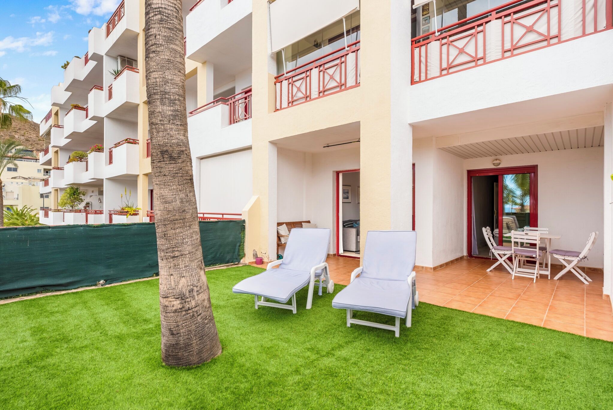 A hotel with a covered outdoor area featuring two lounge chairs and a table.