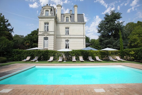 A large building with a swimming pool, lounge chairs, and umbrellas. - Château La Comtesse de Loire & Spa (Saumur)