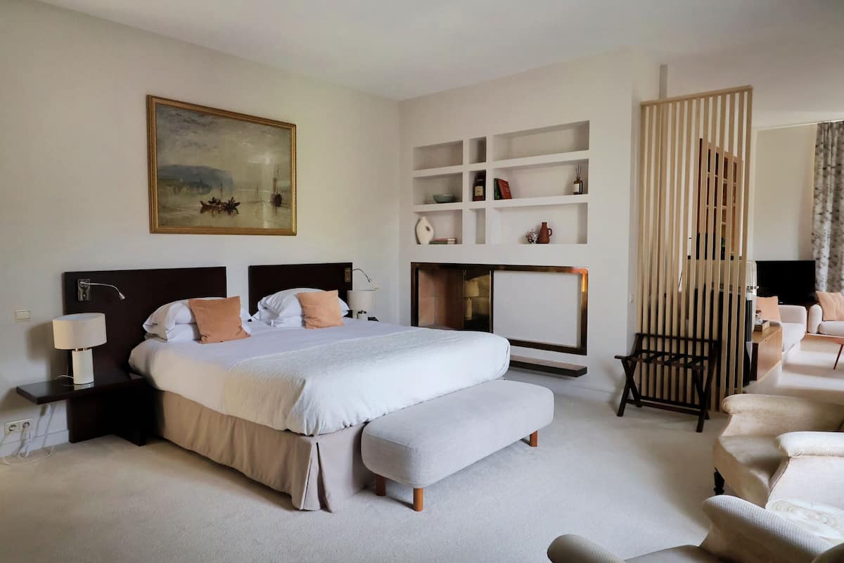 A modern hotel room with a large bed, a bench, a TV, and a bookshelf.