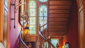 Una imponente escalera con barandales ornamentados y vidrieras de colores.