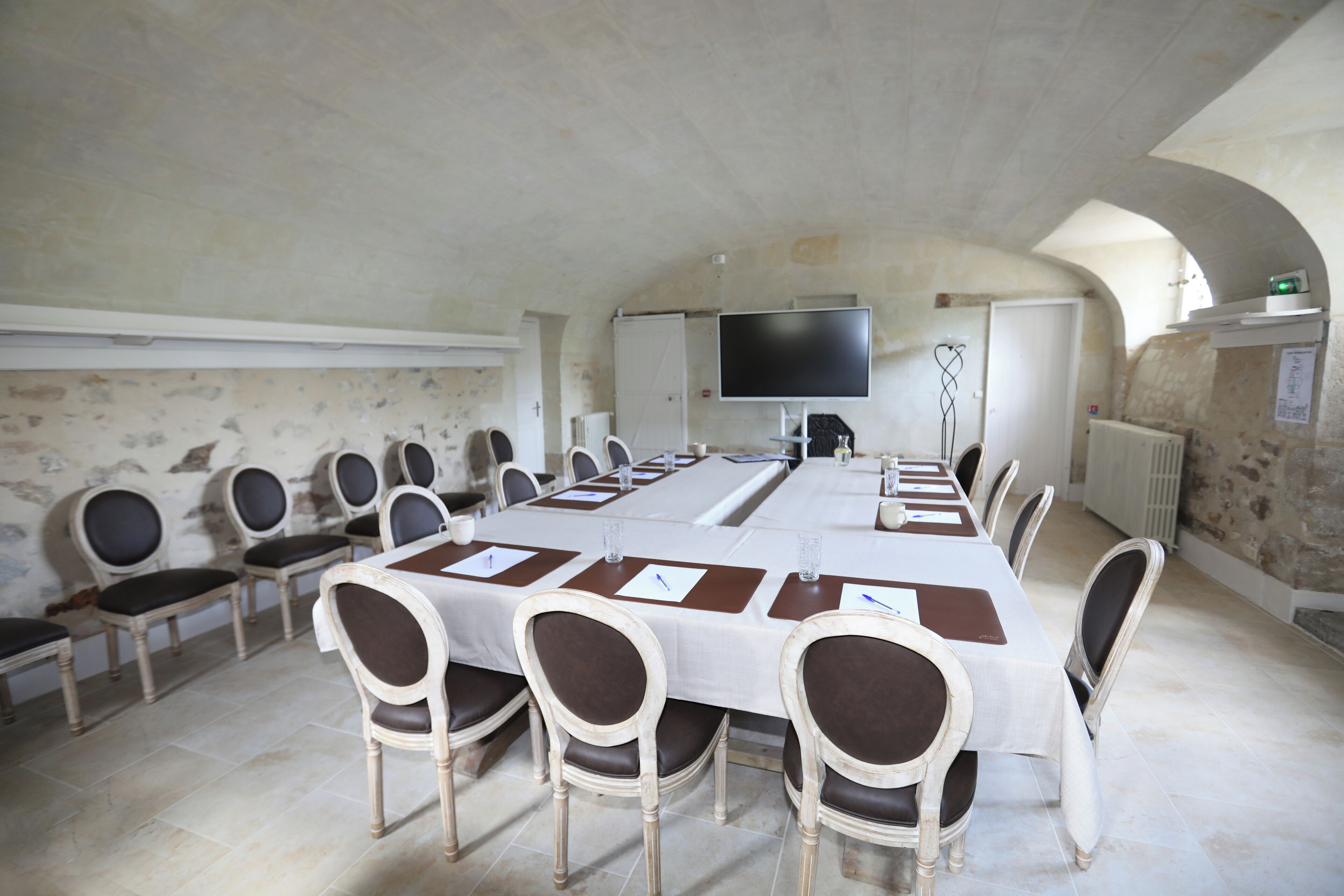 A conference room with a long table, chairs, a flat-screen TV, and a whiteboard.