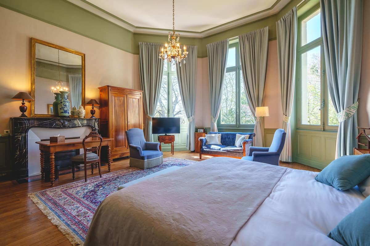 A bedroom with a large bed, a television, a desk with a chair, and a sofa.