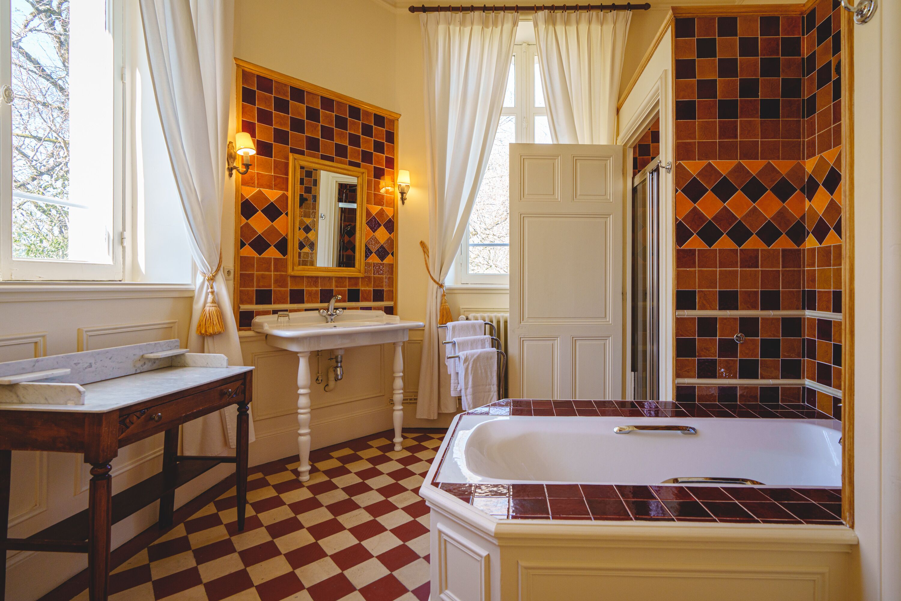 Ein Badezimmer mit Schachbrettboden, einem Waschbecken, einem Spiegel, einer Badewanne und einer Tür.