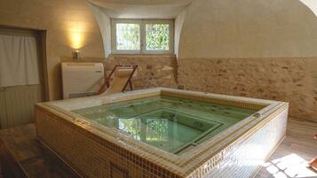 A room with a large tiled hot tub, a window with bars, and a radiator.