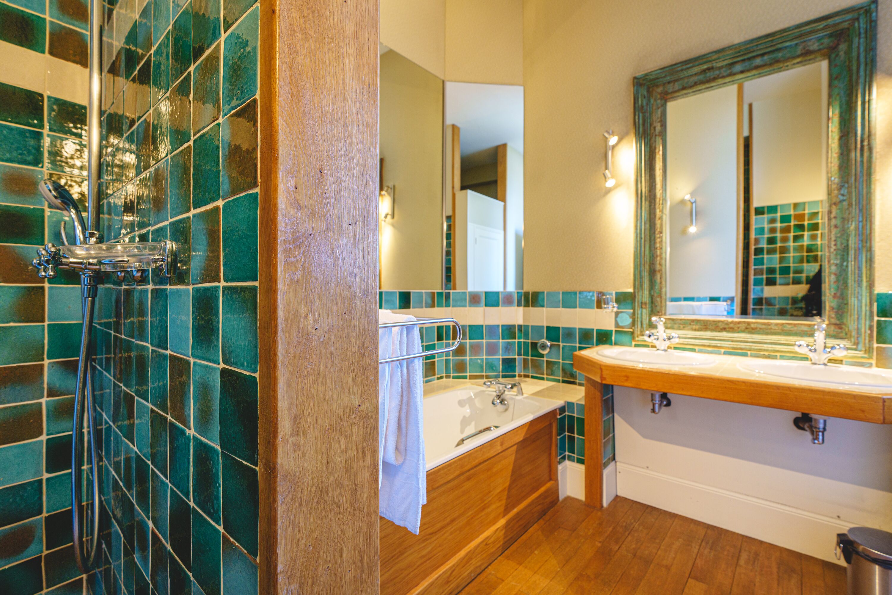 Een badkamer met een houten bad, een wastafel met spiegel en een douche met glazen deur.
