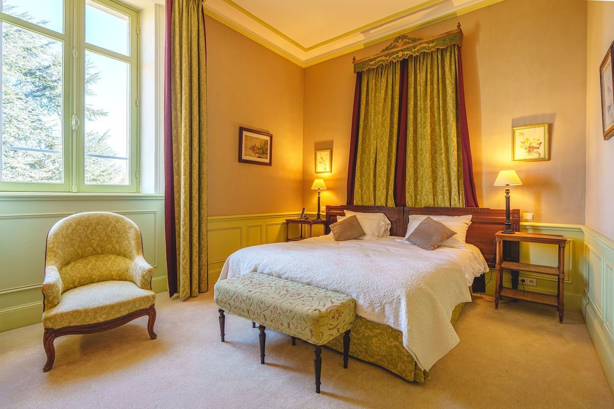A bedroom with a large bed, two bedside tables with lamps, a chair, and a bench.