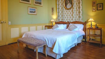 A bedroom with a large bed, a wooden bench, two bedside tables with lamps, and framed pictures on the walls.