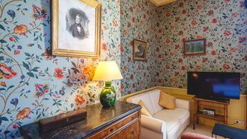 A living room with floral wallpaper, a sofa, a television, and a lamp.