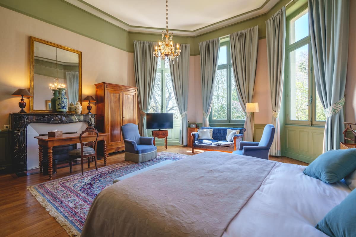 A bedroom with a large bed, a television, a desk with a chair, and a sofa.