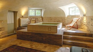 Un cuarto de spa con una amplia tina caliente de azulejos, escalones de madera y dos ventanas con cortinas.