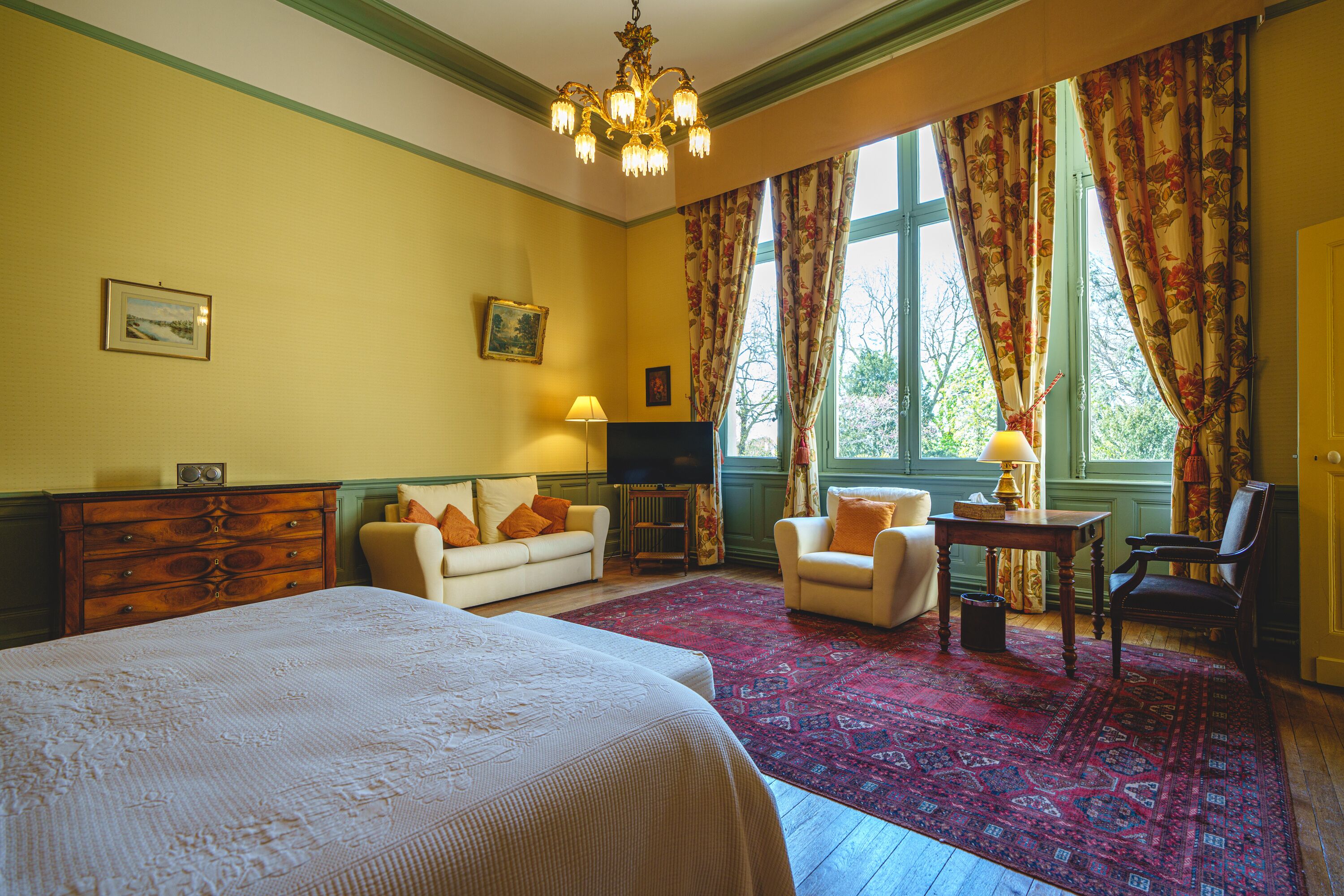 Habitación de hotel con una cama grande, dos sillones, una mesita, un televisor y una ventana con cortinas.
