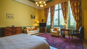 Habitación de hotel con una cama grande, dos sillones, una mesita, un televisor y una ventana con cortinas.