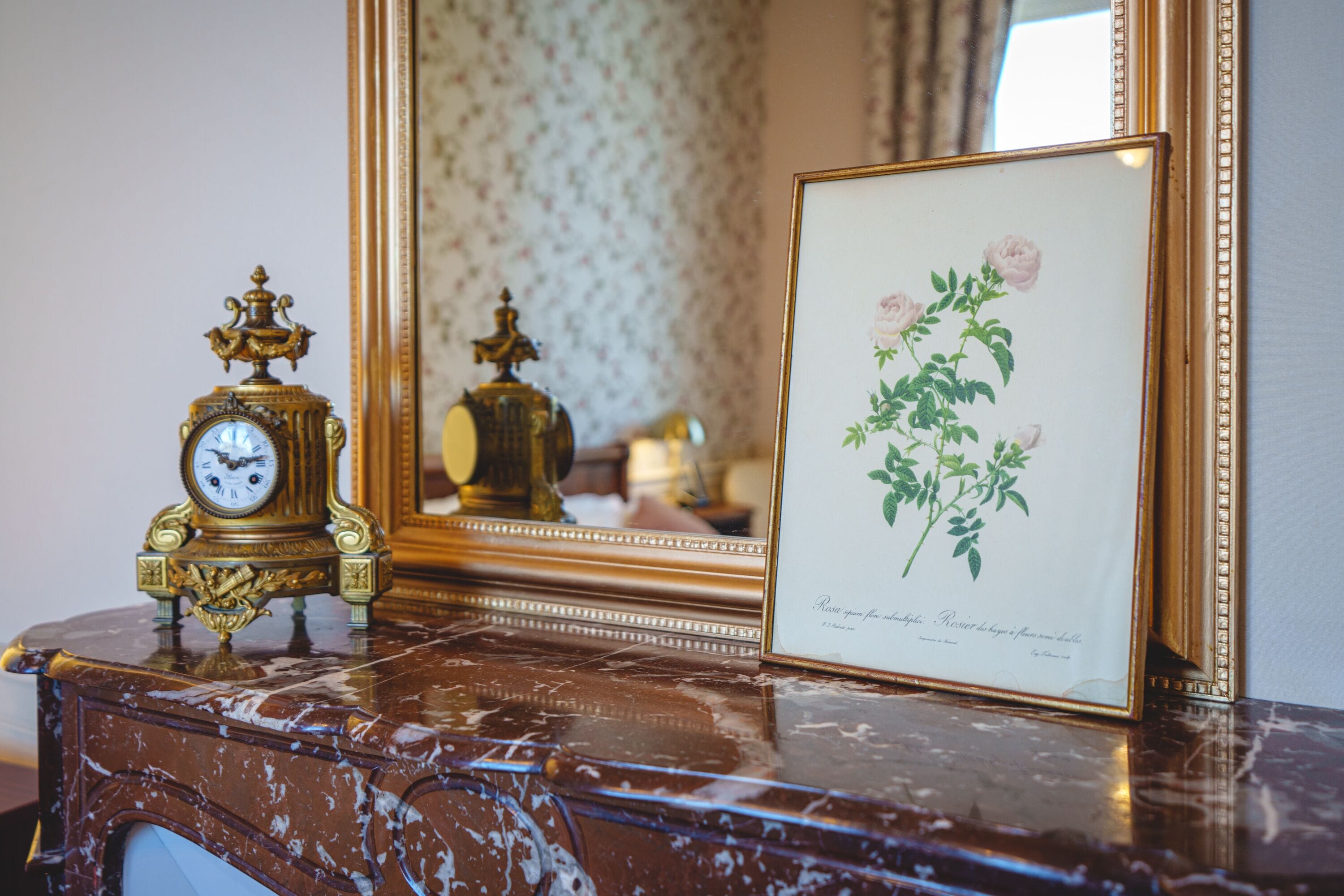 A marble table with a framed botanical print and a decorative clock.