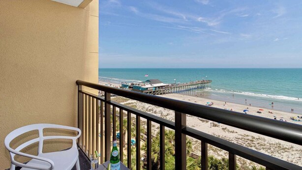 Ein Balkon mit Blick auf einen Strand, einen Steg und einen klaren Himmel.