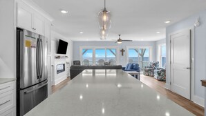 A modern kitchen with a large island, stainless steel appliances, and a view of the ocean through large windows. - Waves of Joy: Oceanfront Home with Elevated Pool and Elevator (Oak Island)