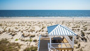 A beach house with a wooden deck and a blue roof overlooking the ocean. - Waves of Joy: Oceanfront Home with Elevated Pool and Elevator (Oak Island)