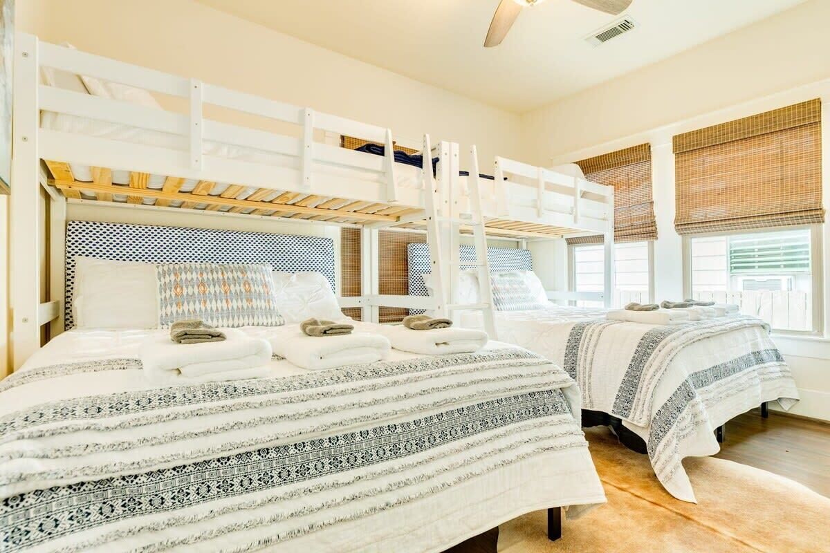 A hotel room with bunk beds, a large bed with patterned bedding, and a view of the outdoors through the windows.