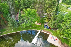 Vue aérienne d’une propriété comprenant une piscine, un petit quai et un jardin avec une maison bleue et des chaises rouges.