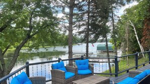 A deck with wicker furniture and blue cushions, overlooking a lake with boats and docked near a forested area. - Spacious Cabin on Whitefish Chain—Perfect for  Family Vacations! (Crosslake)