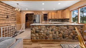 A modern kitchen with a stone island, wooden cabinets, and a large window offering a view of the outdoors. - Spacious Cabin on Whitefish Chain—Perfect for  Family Vacations! (Crosslake)