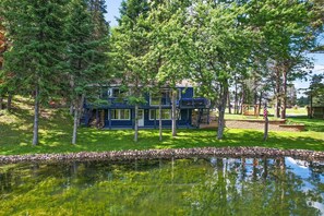 Une maison moderne à deux étages, avec un chemin de pierre menant à un étang, le tout entouré d’une végétation luxuriante et d’arbres.
