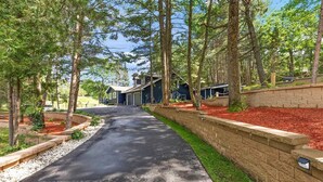 A residential driveway leading to a house with a garage, surrounded by trees and a landscaped garden. - Spacious Cabin on Whitefish Chain—Perfect for  Family Vacations! (Crosslake)