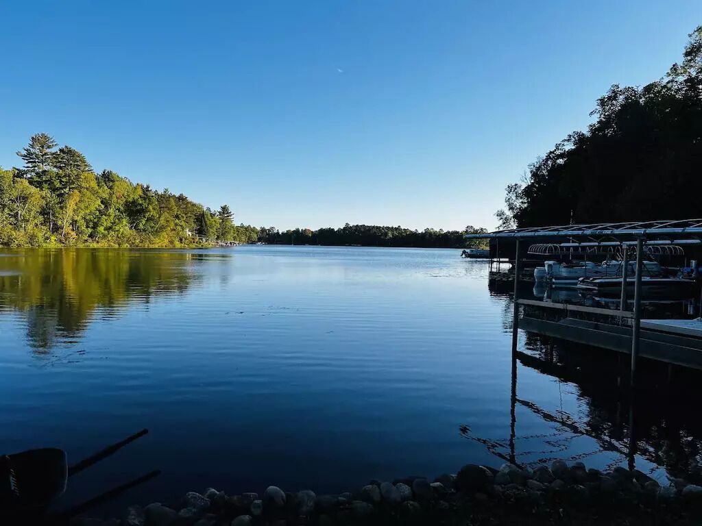 Ein ruhiger See mit einer Anlegestelle und Booten, umgeben von Bäumen.