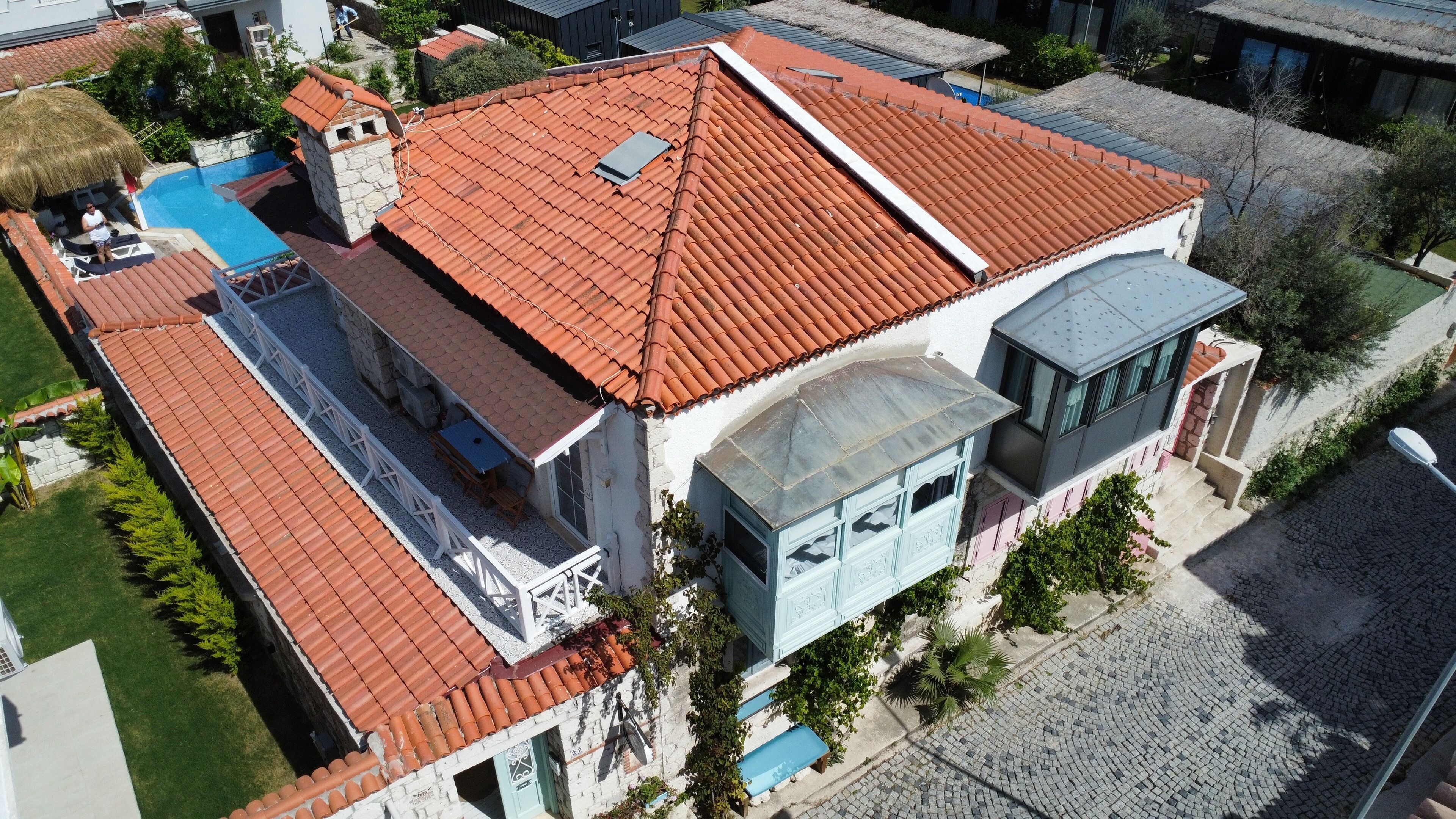 Un edificio de dos pisos con techo de tejas rojas, una chimenea de piedra y una piscina.