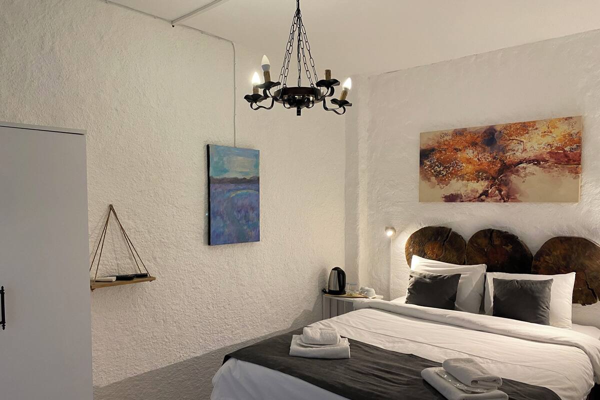 A bedroom with a bed, a painting, a chandelier, and a wooden headboard.