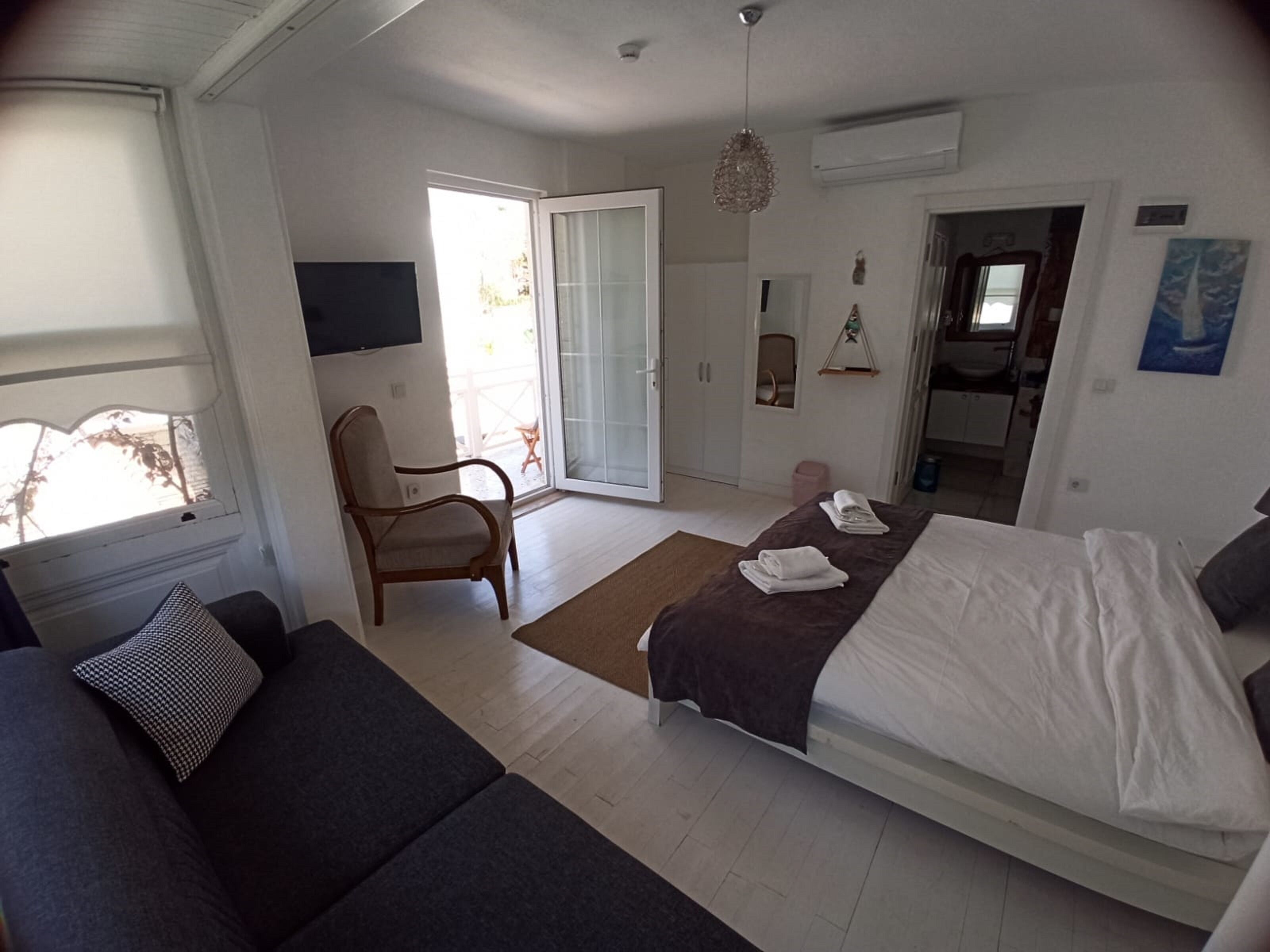 A bedroom with a bed, a sofa, a chair, and a TV.