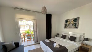 A bedroom with a bed, a bedside table, a lamp, a painting, and a view of an outdoor area with a table and chairs. - Nidus Alaçatı  (Cesme)