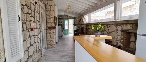 Una cocina con paredes de piedra, encimera de madera y vistas a través de una puerta.