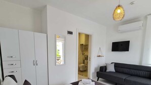 A modern hotel room with a large bed, a sofa, a TV, and a bathroom visible through an open door. - Nidus Alaçatı  (Cesme)