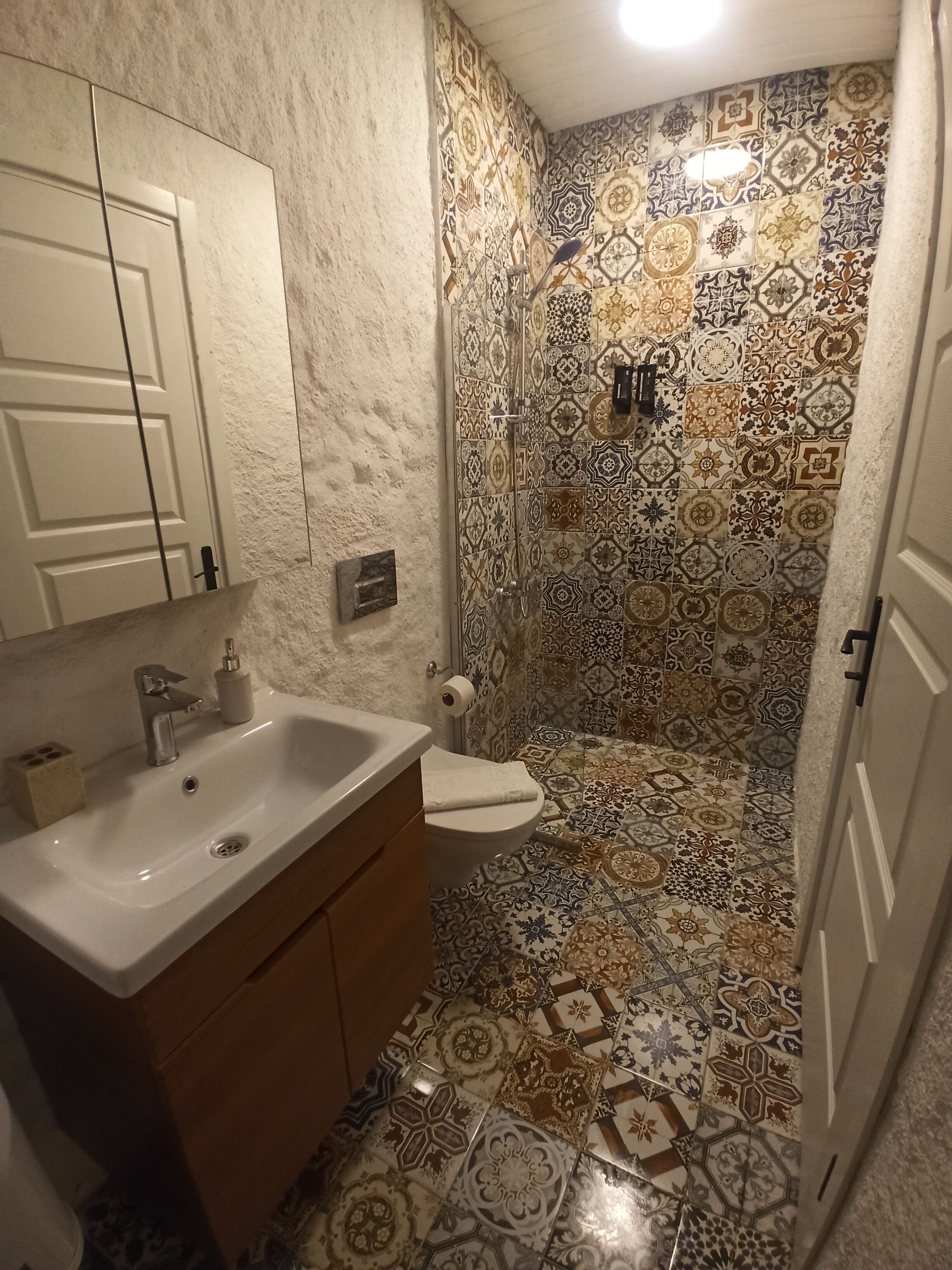 A bathroom with a sink, toilet, and shower. The walls are tiled with a patterned design.