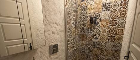A bathroom with a sink, toilet, and shower. The walls are tiled with a patterned design.