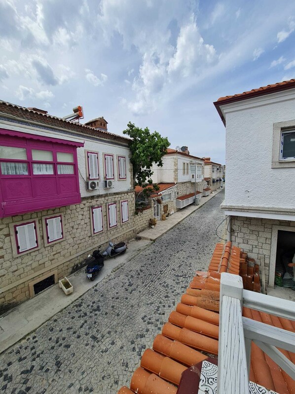 Una calle adoquinada flanqueada por edificios tradicionales, algunos con contraventanas rosadas, y una moto estacionada al lado.