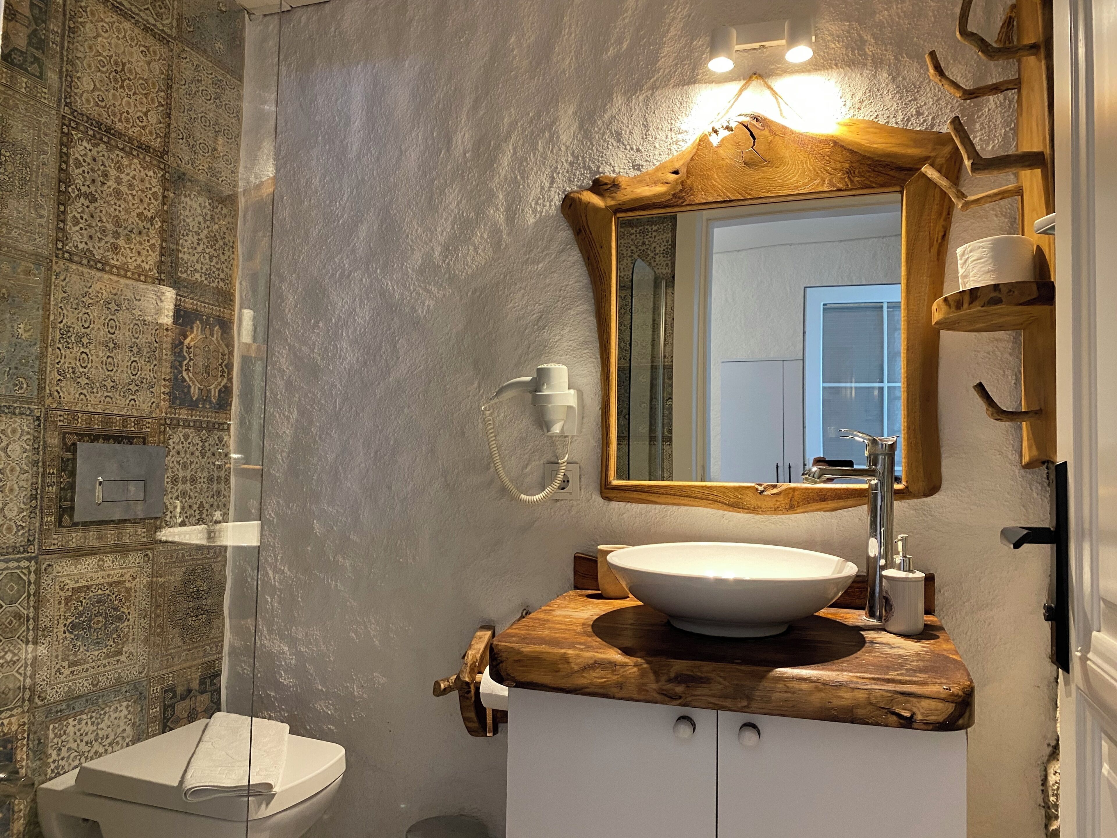 Un baño con un espejo grande, un tocador de madera, un lavabo blanco y un inodoro.