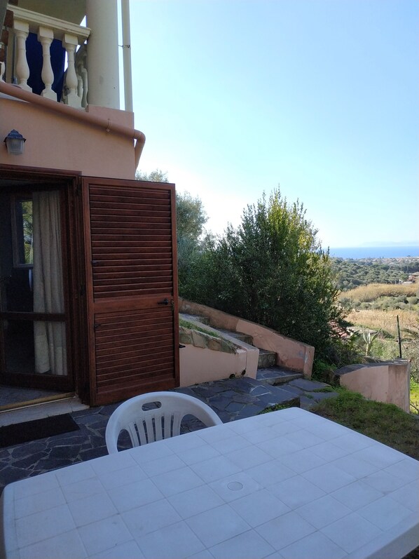 A terrace with a table and chairs, a wooden door, and a view of the landscape.