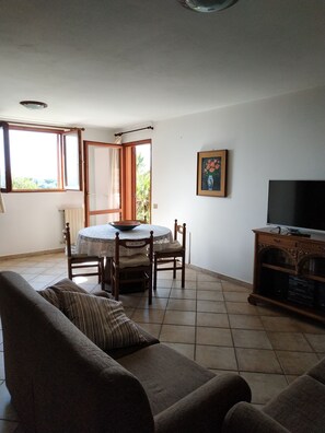 A living room with a sofa, a dining table with chairs, a TV, and a painting on the wall.