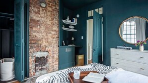 Une chambre avec une cheminée en briques, un lit avec une table de chevet et une commode avec un miroir.