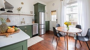Une cuisine avec des meubles de rangement verts, un réfrigérateur en acier inoxydable et un coin repas comprenant une table ronde et des chaises noires.