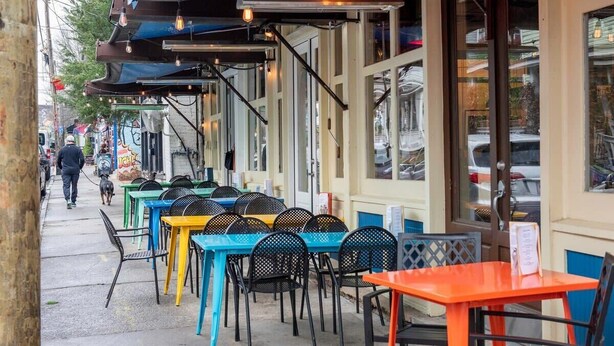 Un espace extérieur aménagé avec des tables et des chaises, un trottoir et un bâtiment doté de grandes fenêtres.