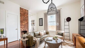 Un salon avec un mur en briques, une cheminée, un canapé, une table basse et un lustre.