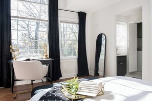 A bedroom with a bed, a desk, a chair, a mirror, and a window with curtains.