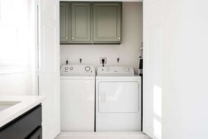 A laundry room with two white washing machines and a dryer, green cabinets above, and a white countertop to the left. - Checkmate (Atlanta)