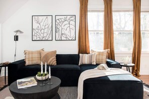 A modern living room with a black sofa, a round coffee table, and two framed wall art pieces.