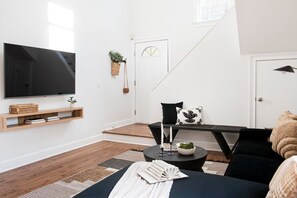 A modern living room with a flat-screen TV, a black sofa, a coffee table, and a staircase leading to another room.